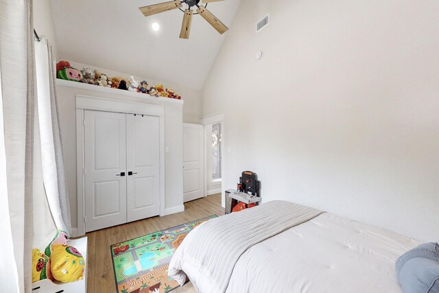 bedroom featuring ceiling fan, high vaulted ceiling, light wood-style flooring, visible vents, and a closet