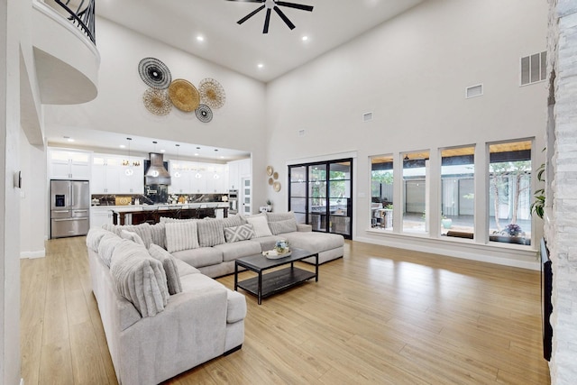 living room featuring visible vents, a towering ceiling, ceiling fan, and light wood-type flooring