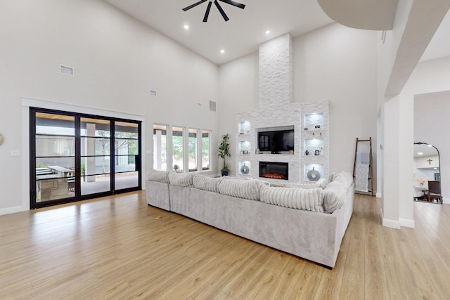 living area with ceiling fan, a high ceiling, light wood finished floors, a fireplace, and visible vents