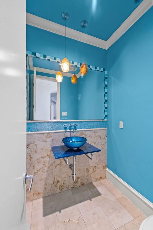 bathroom with a wainscoted wall, a sink, tile walls, and ornamental molding