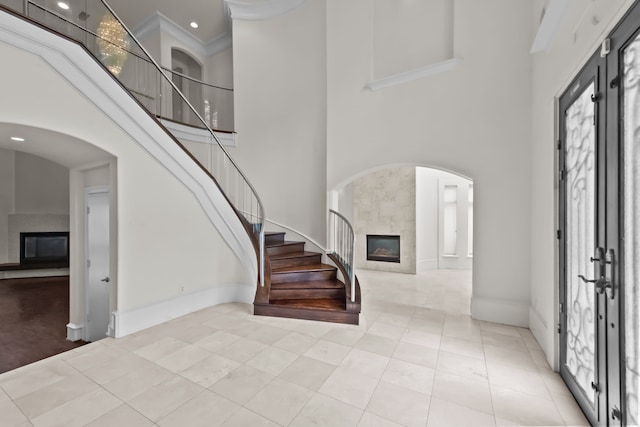 tiled entryway featuring baseboards, a high ceiling, stairway, a tile fireplace, and arched walkways