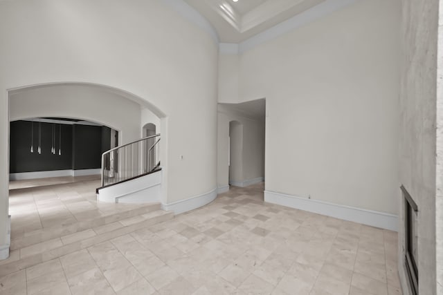 unfurnished living room with arched walkways, baseboards, and a towering ceiling