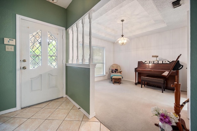 foyer entrance with visible vents, a tray ceiling, a notable chandelier, and baseboards