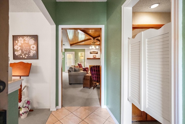 corridor featuring light tile patterned floors, a textured ceiling, light carpet, and baseboards