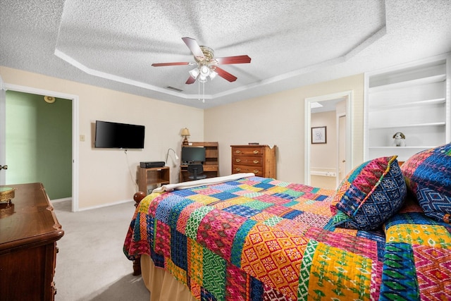 carpeted bedroom featuring a raised ceiling, a ceiling fan, visible vents, baseboards, and a textured ceiling