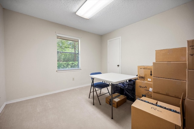 office area with a textured ceiling, baseboards, and light carpet