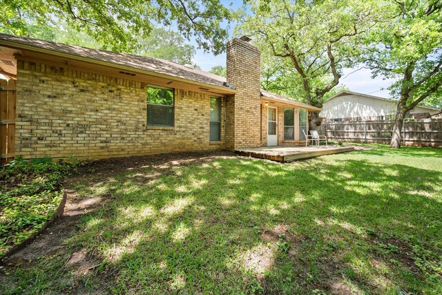 rear view of property featuring a chimney, a lawn, brick siding, a deck, and fence