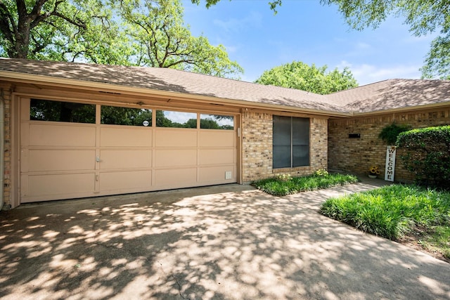 ranch-style house with brick siding, roof with shingles, concrete driveway, and an attached garage