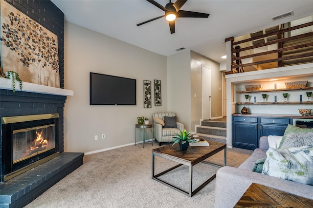carpeted living room featuring visible vents, a brick fireplace, baseboards, ceiling fan, and stairway