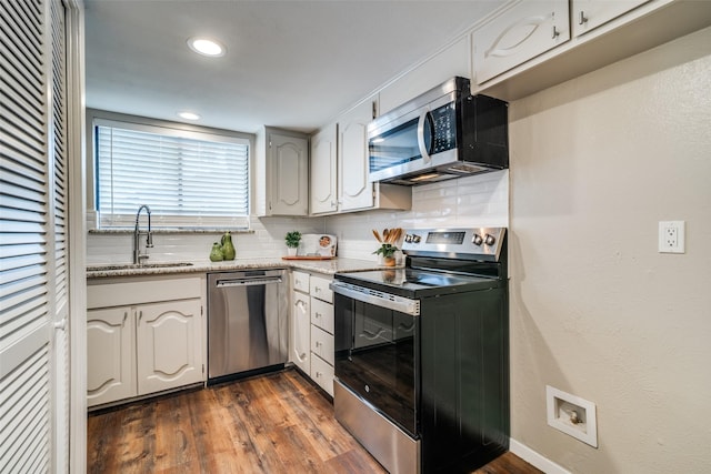 kitchen featuring dark wood-style flooring, tasteful backsplash, a sink, light stone counters, and stainless steel appliances