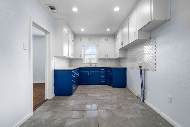 kitchen featuring visible vents, blue cabinets, white cabinetry, and backsplash
