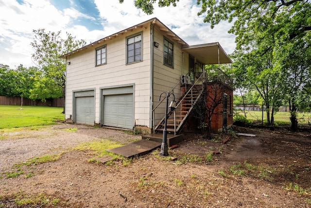 view of side of home with a garage, stairway, a yard, dirt driveway, and fence