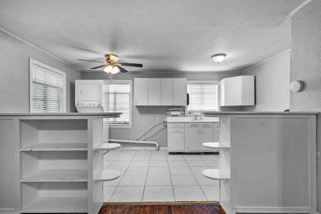 kitchen with open shelves, white cabinets, stacked washer and clothes dryer, ceiling fan, and a wealth of natural light