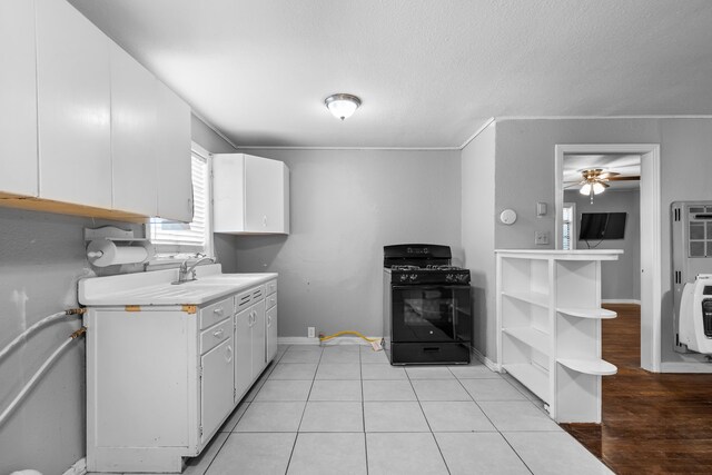 kitchen with a sink, black gas stove, heating unit, ceiling fan, and light countertops