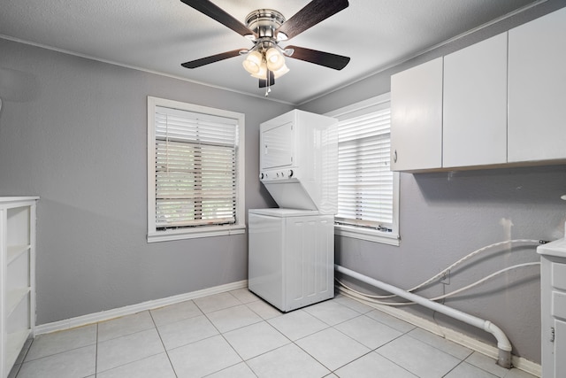 clothes washing area with a ceiling fan, cabinet space, stacked washer and clothes dryer, and a healthy amount of sunlight