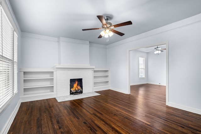 unfurnished living room featuring baseboards, wood finished floors, ceiling fan, and a brick fireplace