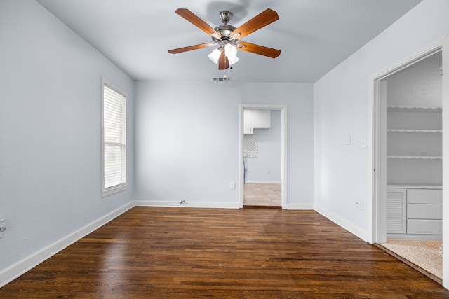 unfurnished bedroom with a ceiling fan, ensuite bath, dark wood finished floors, and baseboards