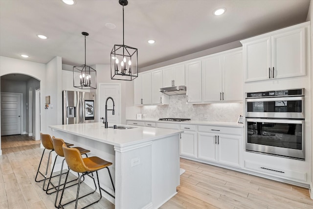 7100 Dandelion Dr, Little Elm, TX 76227 - kitchen featuring stainless steel appliances, a sink, light wood-style flooring, arched walkways, and recessed lighting