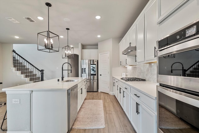 kitchen with stainless steel appliances, light wood-style floors, under cabinet range hood, a sink, and visible vents