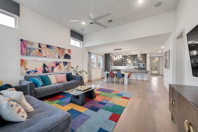 living room with recessed lighting, light wood-type flooring, visible vents, a ceiling fan, and a high ceiling