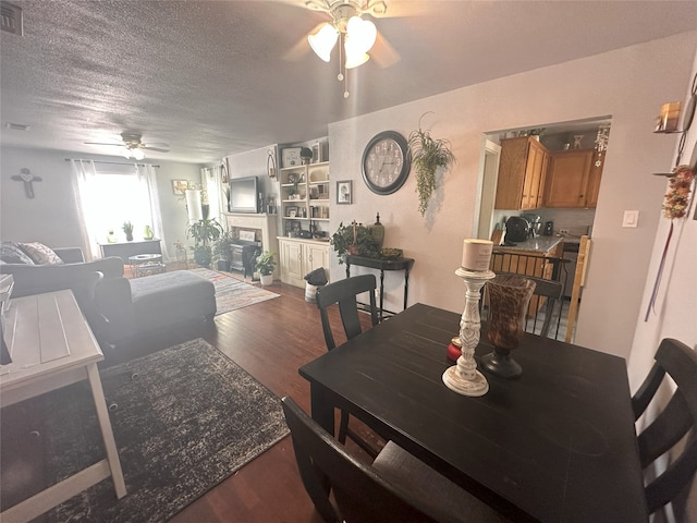 dining space featuring wood finished floors, ceiling fan, a textured ceiling, and a fireplace