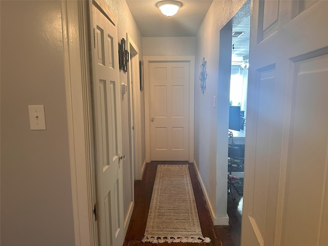corridor featuring baseboards and dark wood-type flooring