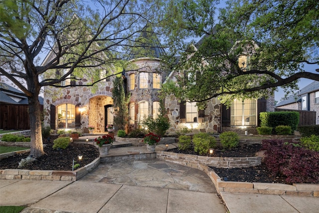 view of front of property with a patio, fence, and stone siding