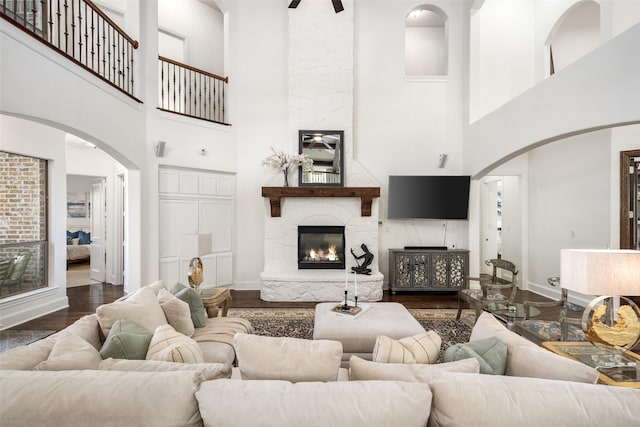 living room with a towering ceiling, wood finished floors, stairway, a high end fireplace, and arched walkways