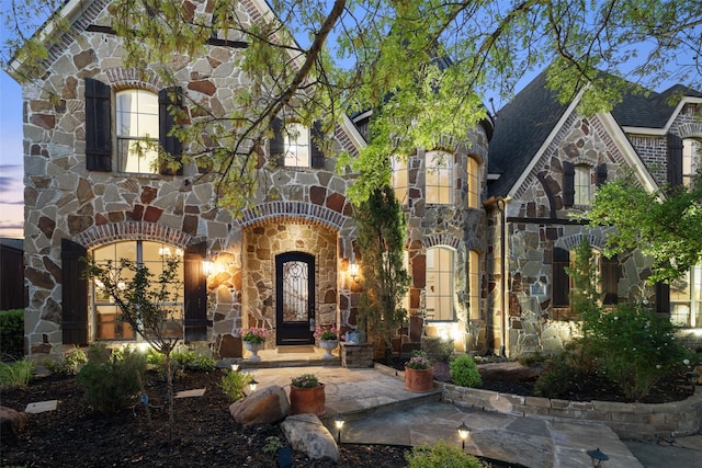 view of front of property with a shingled roof and stone siding