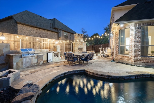 view of swimming pool featuring an outdoor kitchen, grilling area, a fenced backyard, exterior fireplace, and a patio