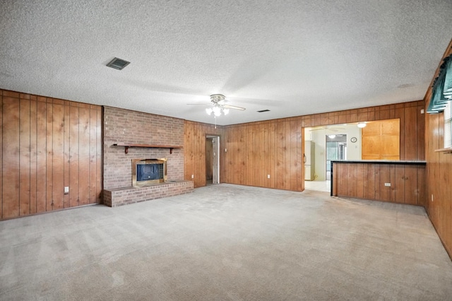 2134 Braune Rd, Abilene, TX 79606 - unfurnished living room with wood walls, light colored carpet, ceiling fan, a textured ceiling, and a brick fireplace