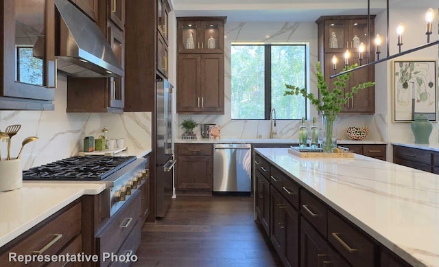 kitchen with tasteful backsplash, a sink, stainless steel appliances, under cabinet range hood, and dark wood-style flooring