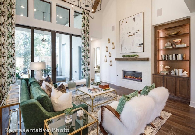 living room featuring baseboards, a towering ceiling, dark wood-type flooring, and a glass covered fireplace