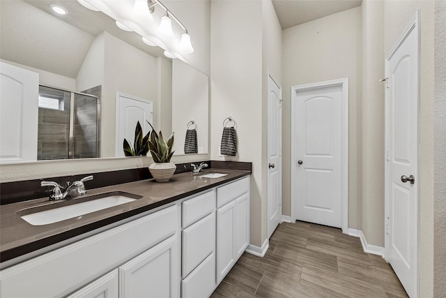 full bath featuring a sink, baseboards, a shower stall, and double vanity
