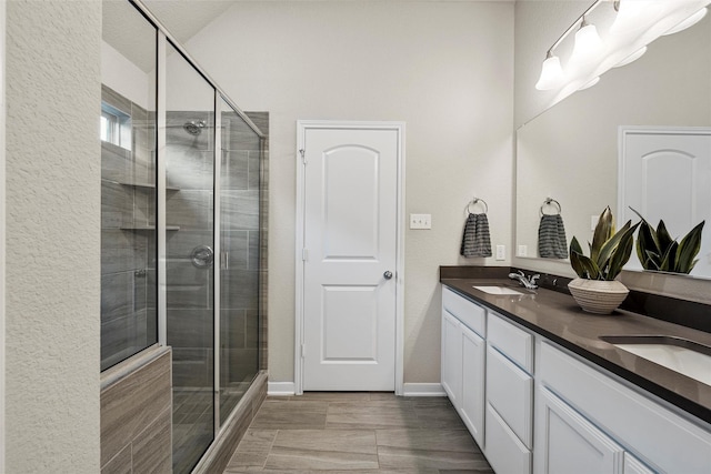bathroom with double vanity, baseboards, a shower stall, and a sink