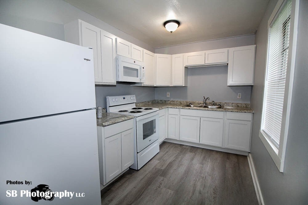 kitchen with wood finished floors, white appliances, white cabinetry, and a sink