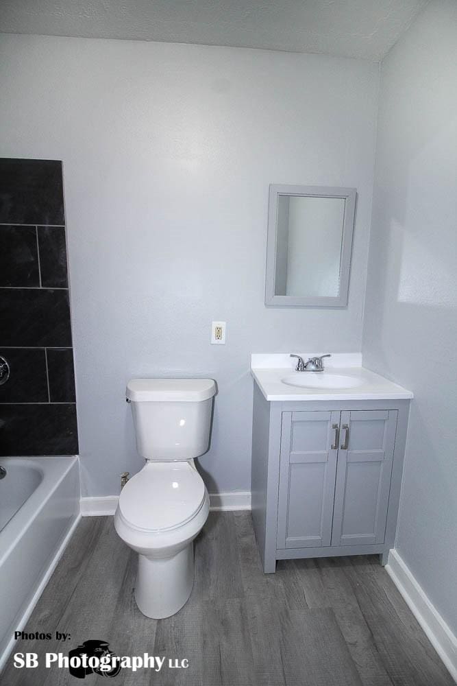full bath with baseboards, wood finished floors, toilet, and vanity