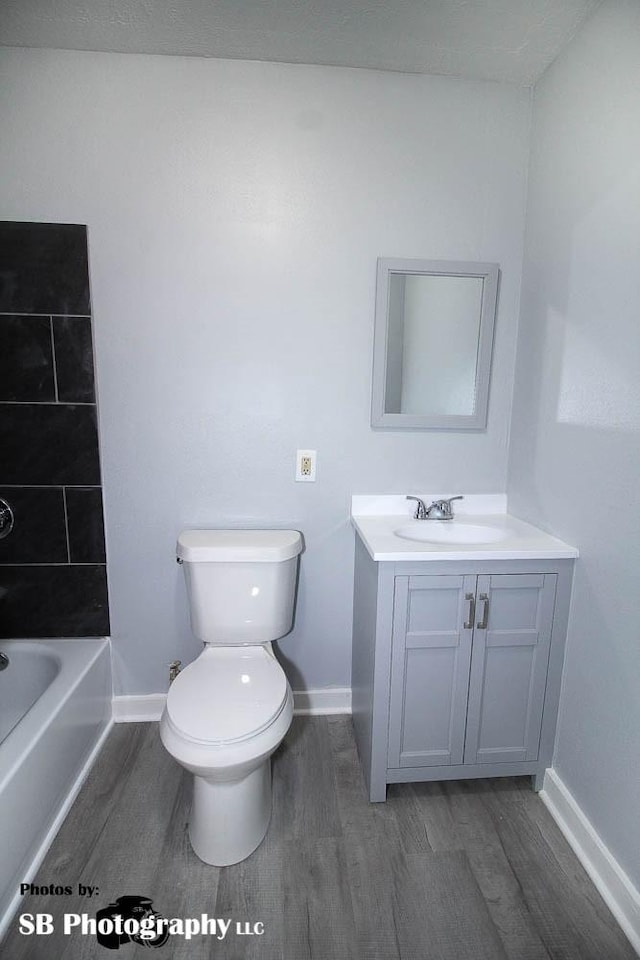 full bath with baseboards, wood finished floors, toilet, and vanity