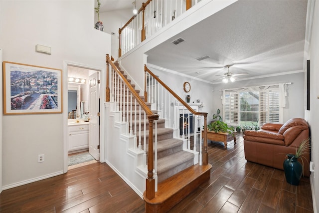stairs featuring wood finished floors, visible vents, a ceiling fan, and ornamental molding