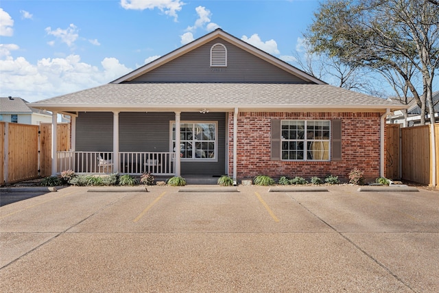 single story home featuring uncovered parking, roof with shingles, covered porch, fence, and brick siding