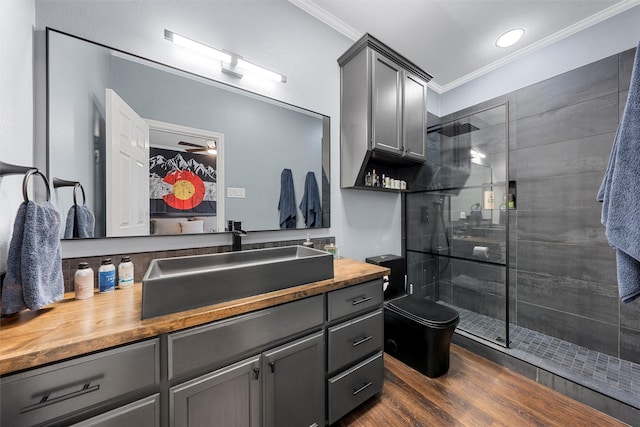 ensuite bathroom featuring wood finished floors, vanity, ornamental molding, and tiled shower