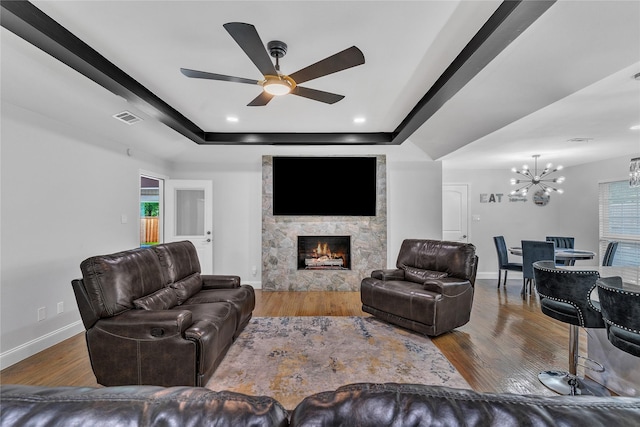 living area with wood finished floors, ceiling fan with notable chandelier, a fireplace, baseboards, and visible vents