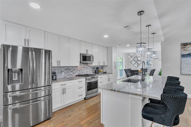 kitchen featuring a kitchen breakfast bar, a sink, visible vents, stainless steel appliances, and light wood-style floors