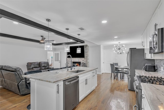 kitchen with a sink, appliances with stainless steel finishes, a warm lit fireplace, open floor plan, and light stone countertops