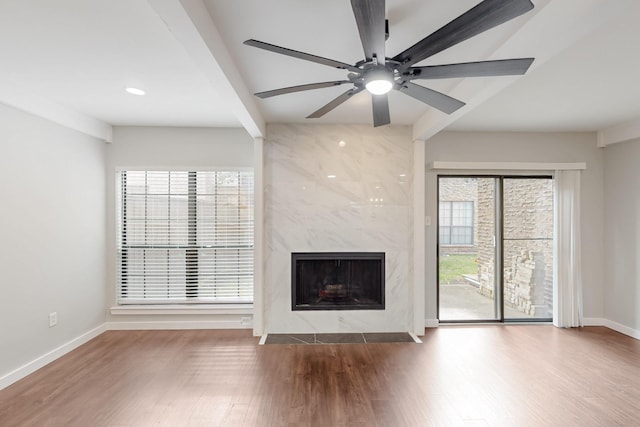 unfurnished living room featuring wood finished floors, a ceiling fan, a high end fireplace, and baseboards