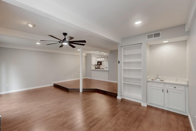 unfurnished living room featuring wood finished floors, visible vents, built in shelves, and baseboards