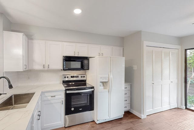 kitchen featuring white refrigerator with ice dispenser, stainless steel electric range, a sink, white cabinetry, and black microwave
