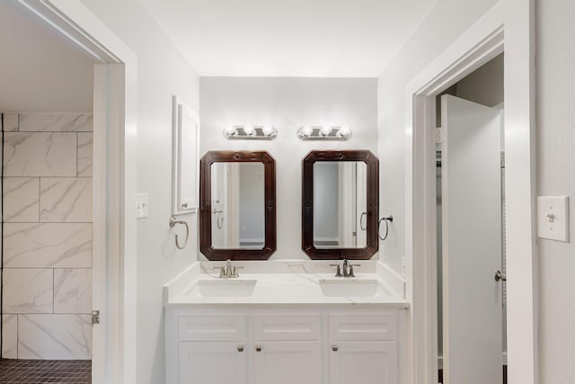 bathroom with tiled shower, double vanity, and a sink