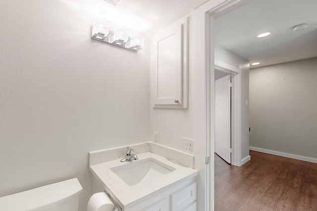 half bathroom featuring recessed lighting, wood finished floors, toilet, vanity, and baseboards