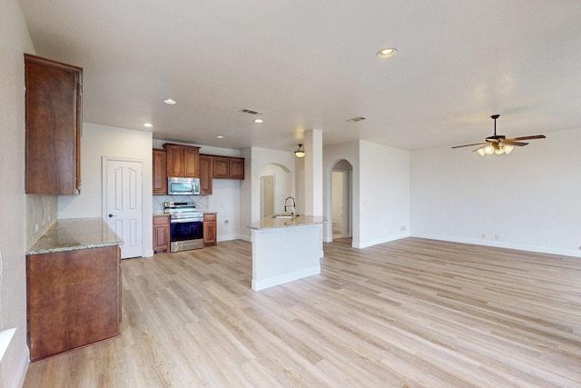 706 Green Leaf Dr, Midlothian, TX 76065 - kitchen featuring appliances with stainless steel finishes, arched walkways, a sink, light wood-style floors, and light stone countertops